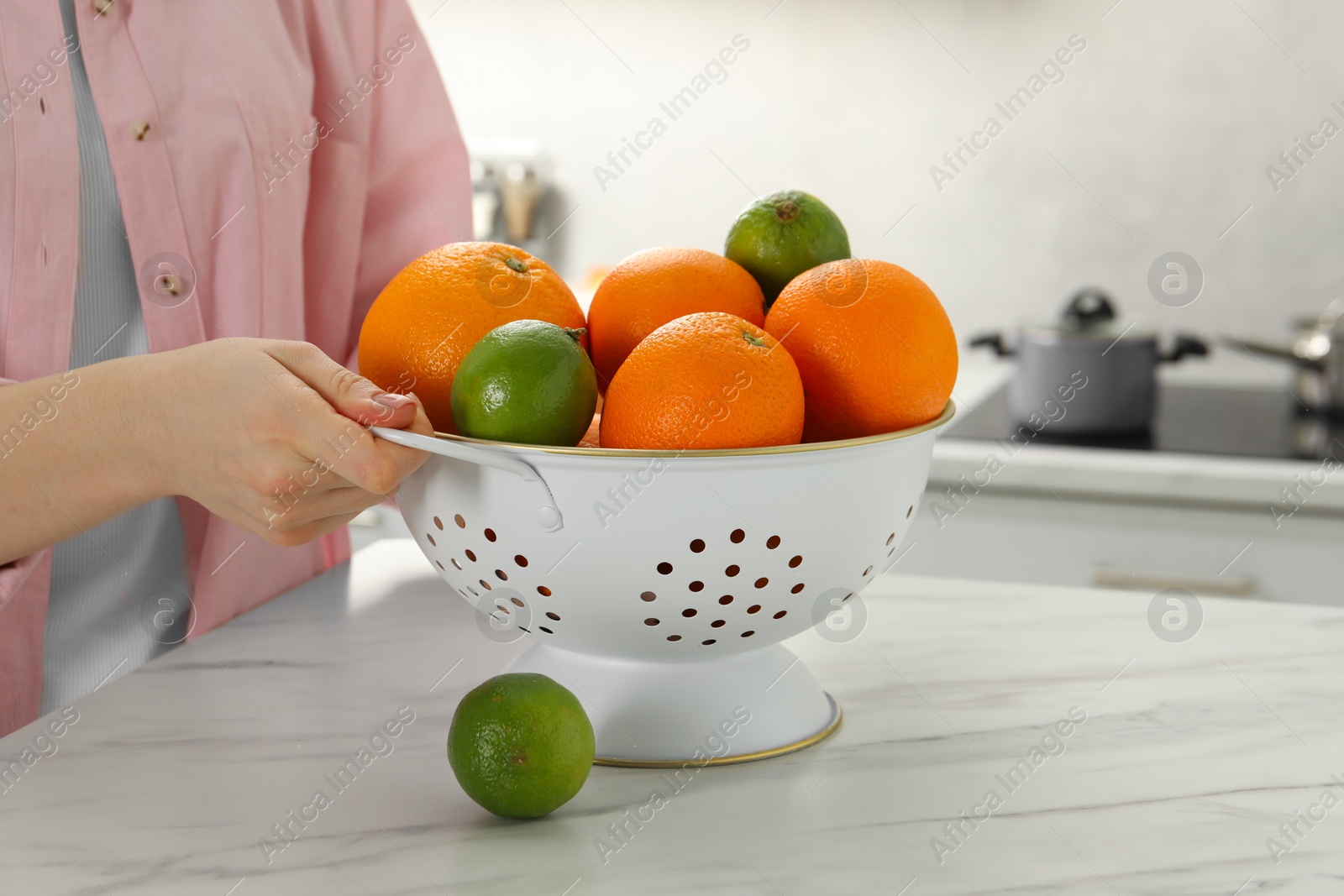 Photo of Woman holding colander with fresh fruits at white marble table in kitchen, closeup