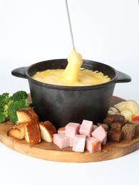 Dipping piece of ham into fondue pot with tasty melted cheese isolated on white