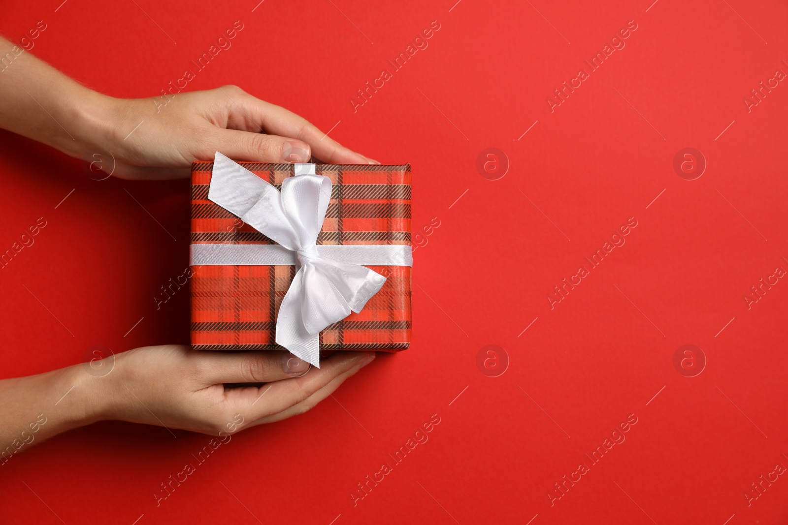 Photo of Woman holding Christmas gift on red background, top view. Space for text