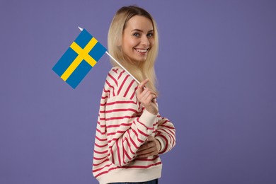 Happy young woman with flag of Sweden on purple background