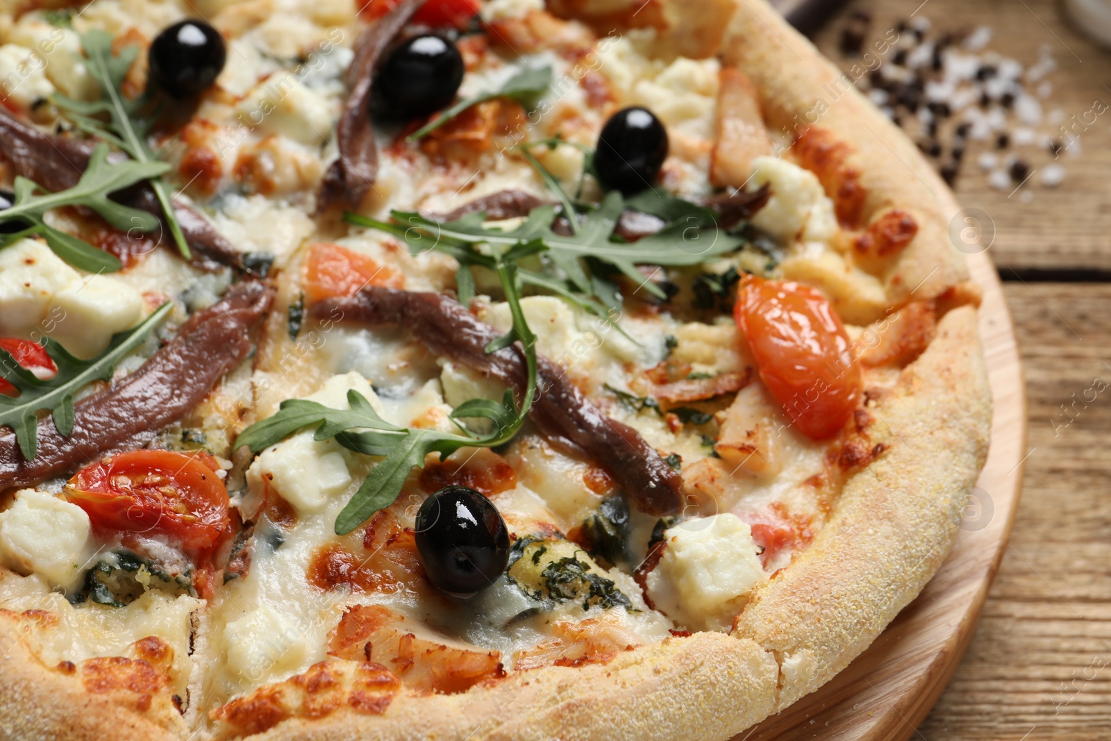 Photo of Tasty pizza with anchovies, arugula and olives on wooden table, closeup