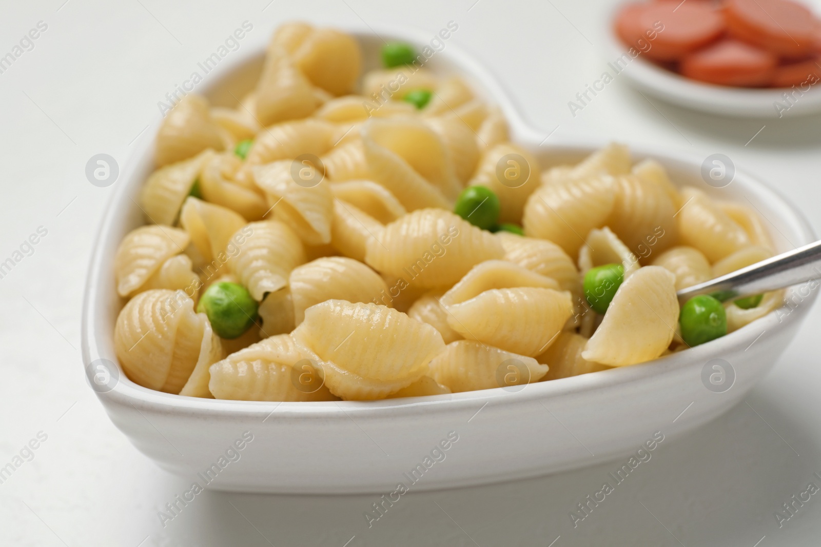 Photo of Heart shaped bowl with tasty pasta and peas on white table, closeup