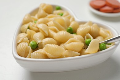 Photo of Heart shaped bowl with tasty pasta and peas on white table, closeup