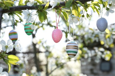 Photo of Beautifully painted Easter eggs hanging on blooming tree outdoors