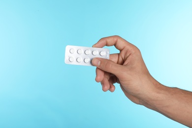 Young man holding pills on color background, closeup with space for text. Medical object