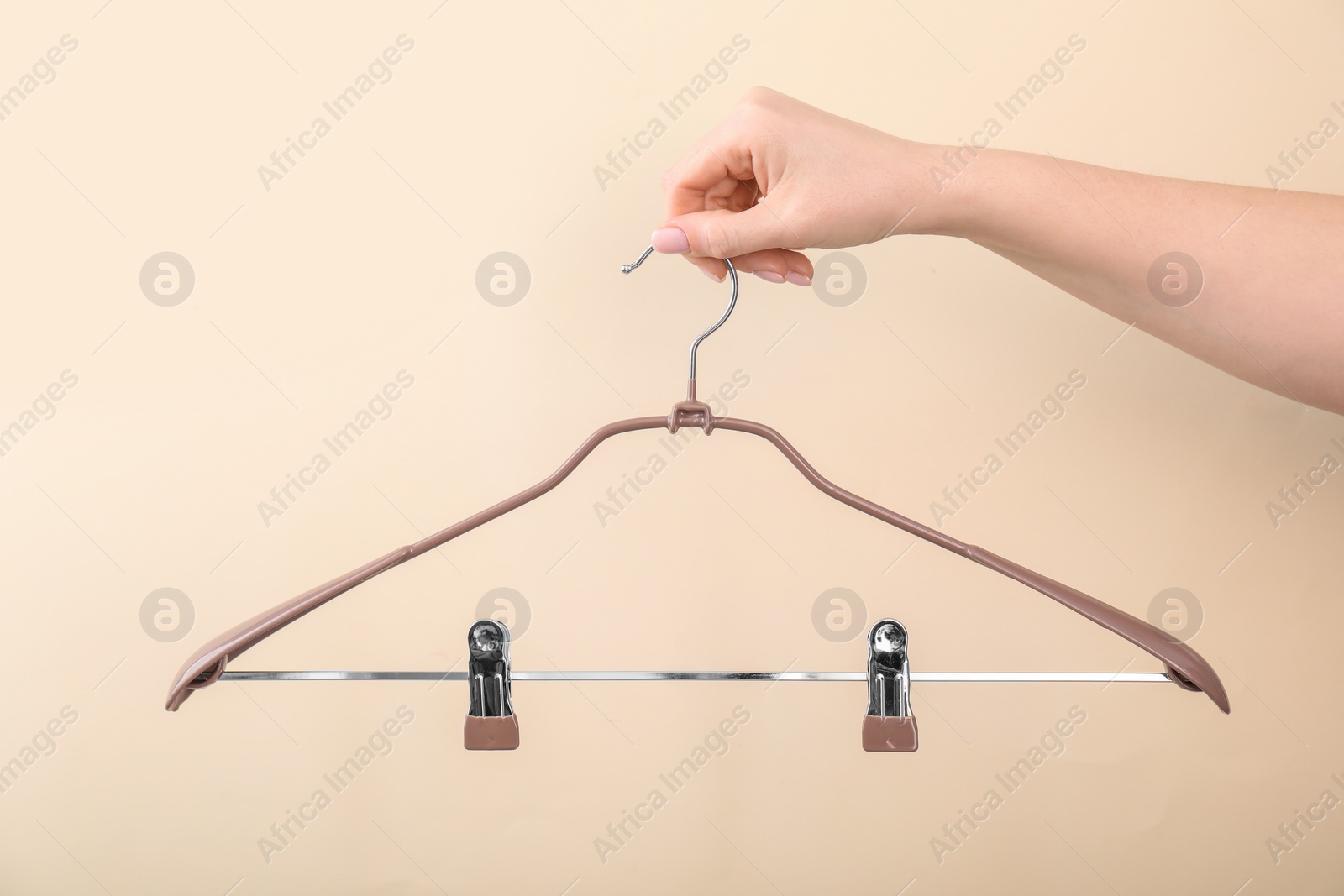 Photo of Woman holding hanger with clips on beige background, closeup