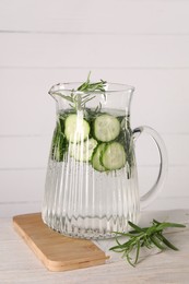 Refreshing cucumber water with rosemary in jug on light wooden table