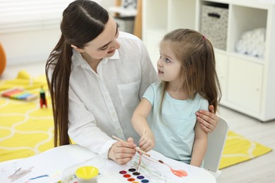 Photo of Mother and her little daughter painting with watercolor at home