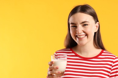 Happy woman with milk mustache holding glass of tasty dairy drink on orange background, space for text