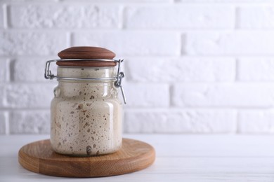 Photo of Sourdough starter in glass jar on white wooden table, space for text