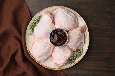 Plate with fresh marinade, raw chicken and rosemary on wooden table, top view