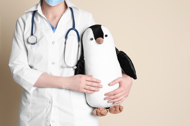 Photo of Pediatrician with toy penguin and stethoscope on beige background, closeup