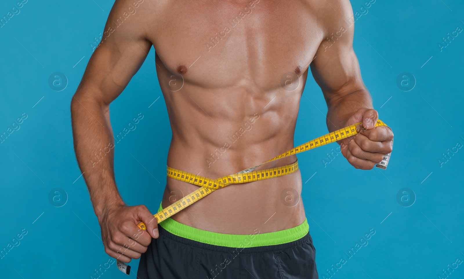 Photo of Shirtless man with slim body and measuring tape around his waist on light blue background, closeup