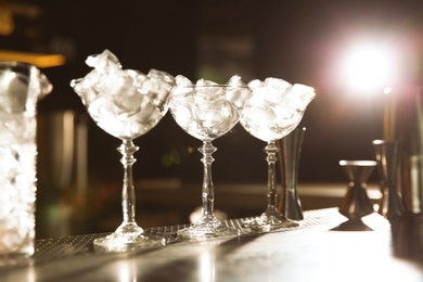 Photo of Martini glasses with ice cubes on bar counter. Space for text