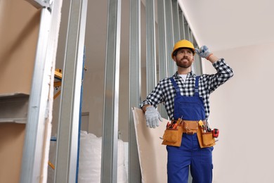 Professional builder in uniform with tool belt indoors