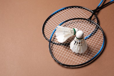 Photo of Feather badminton shuttlecocks and rackets on brown background, space for text