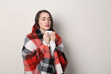 Photo of Young woman with blanket suffering from runny nose on beige background. Space for text