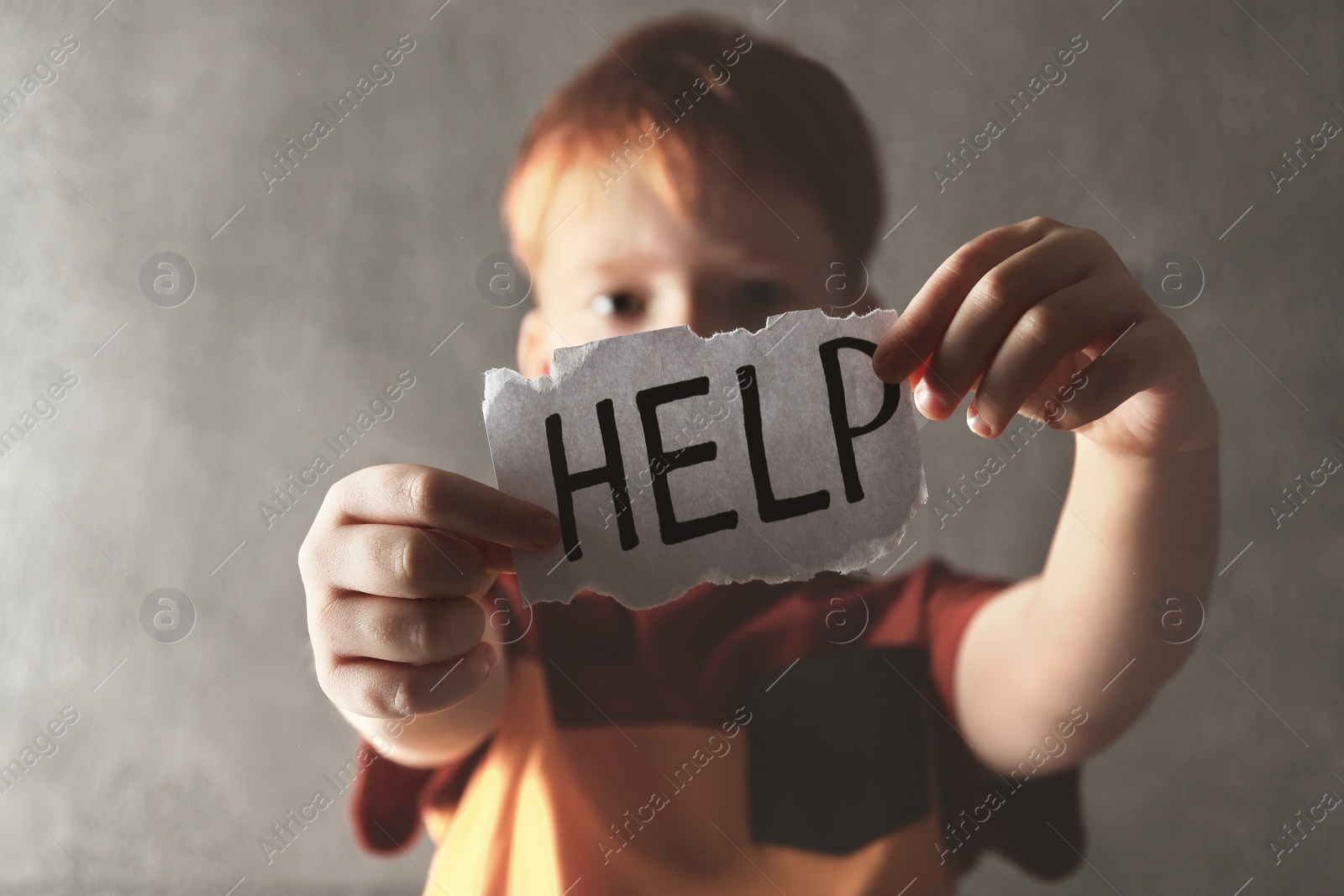 Photo of Little boy holding piece of paper with word Help against light grey background, focus on hands. Domestic violence concept