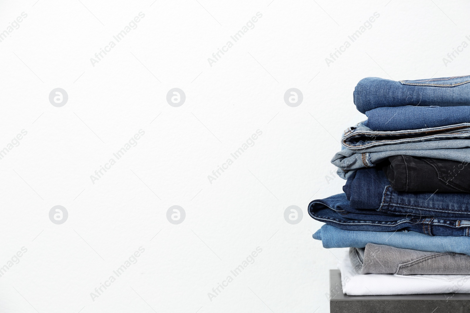 Photo of Stack of different jeans on table against white background. Space for text