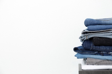 Photo of Stack of different jeans on table against white background. Space for text