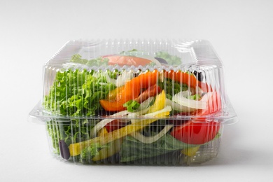 Plastic container with fresh salad on light grey background