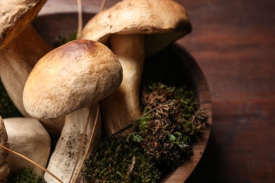 Fresh wild porcini mushrooms in bowl on wooden table, closeup