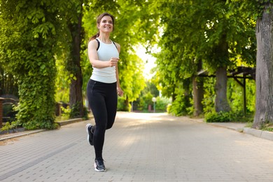 Photo of Young woman with wireless earphones jogging outdoors in morning