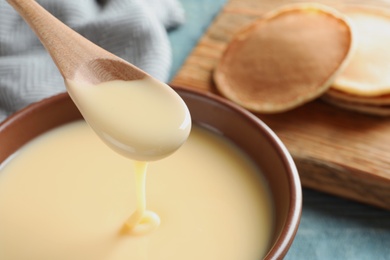 Spoon of pouring condensed milk over bowl on table, closeup with space for text. Dairy products