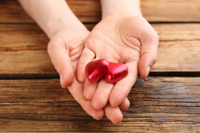 Woman holding heart shaped chocolate candies at wooden table, closeup