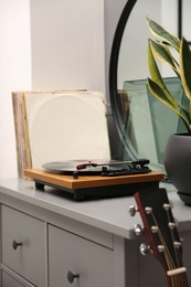 Photo of Stylish turntable with vinyl record on chest of drawers indoors