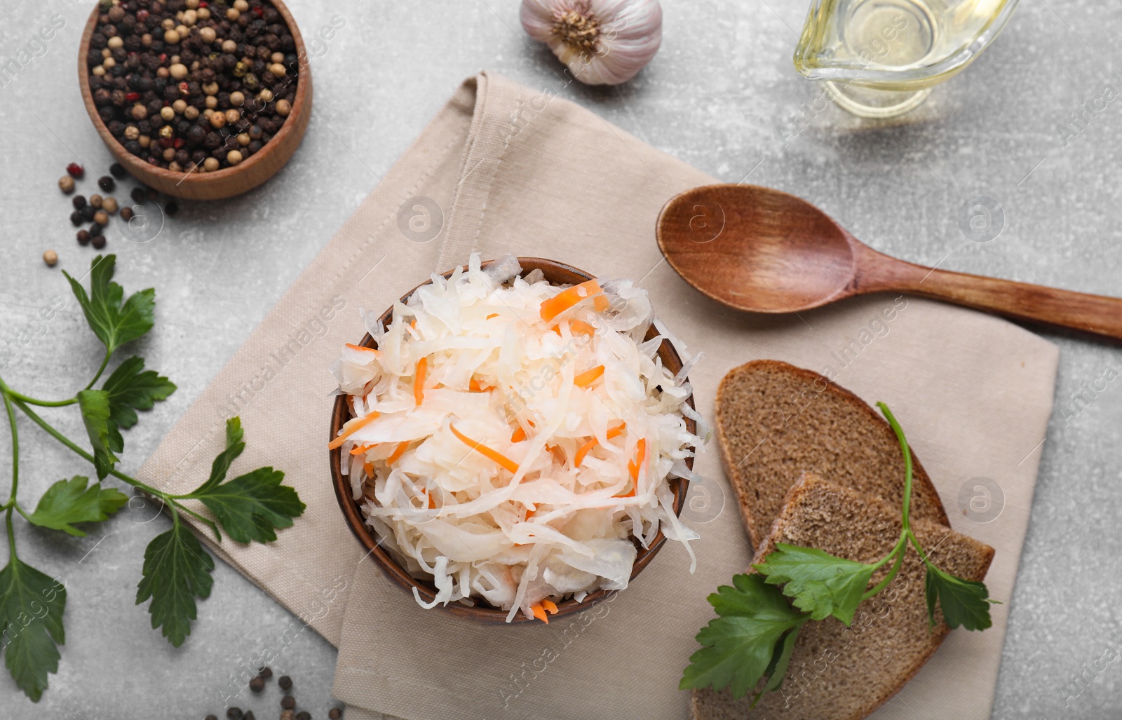 Photo of Bowl of tasty sauerkraut and ingredients on grey table, flat lay