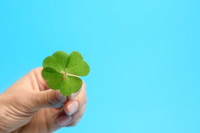 Photo of Woman holding beautiful green four leaf clover on light blue background, closeup. Space for text