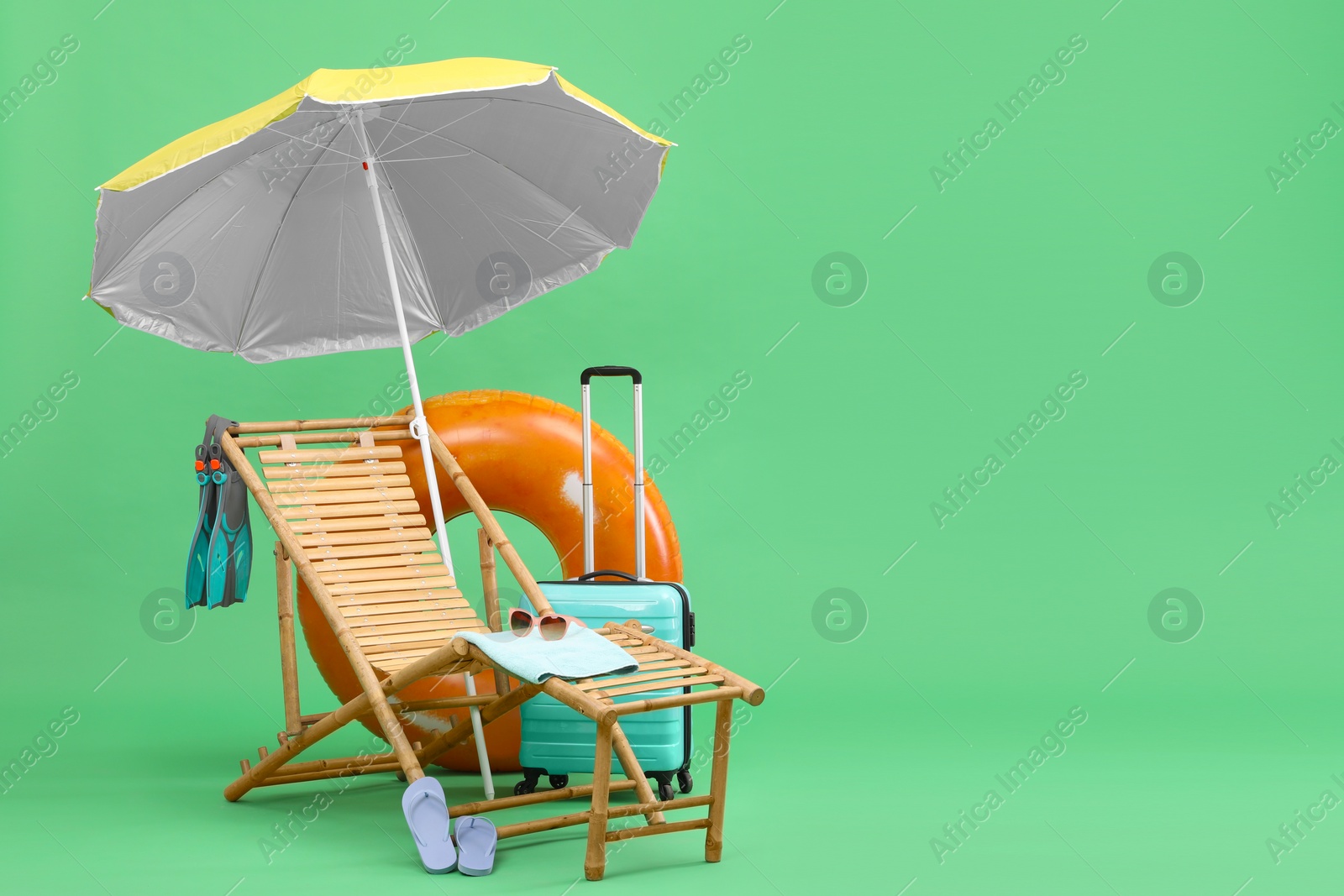 Deck chair, umbrella, suitcase and beach accessories against green background, space for text. Summer vacation Photo of Deck chair, umbrella, suitcase and beach accessories against green background, space for text. Summer vacation