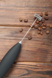 Photo of Black milk frother wand and coffee beans on wooden table, top view