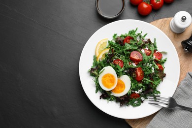Photo of Delicious salad with boiled egg, arugula and tomatoes served on black table, flat lay. Space for text