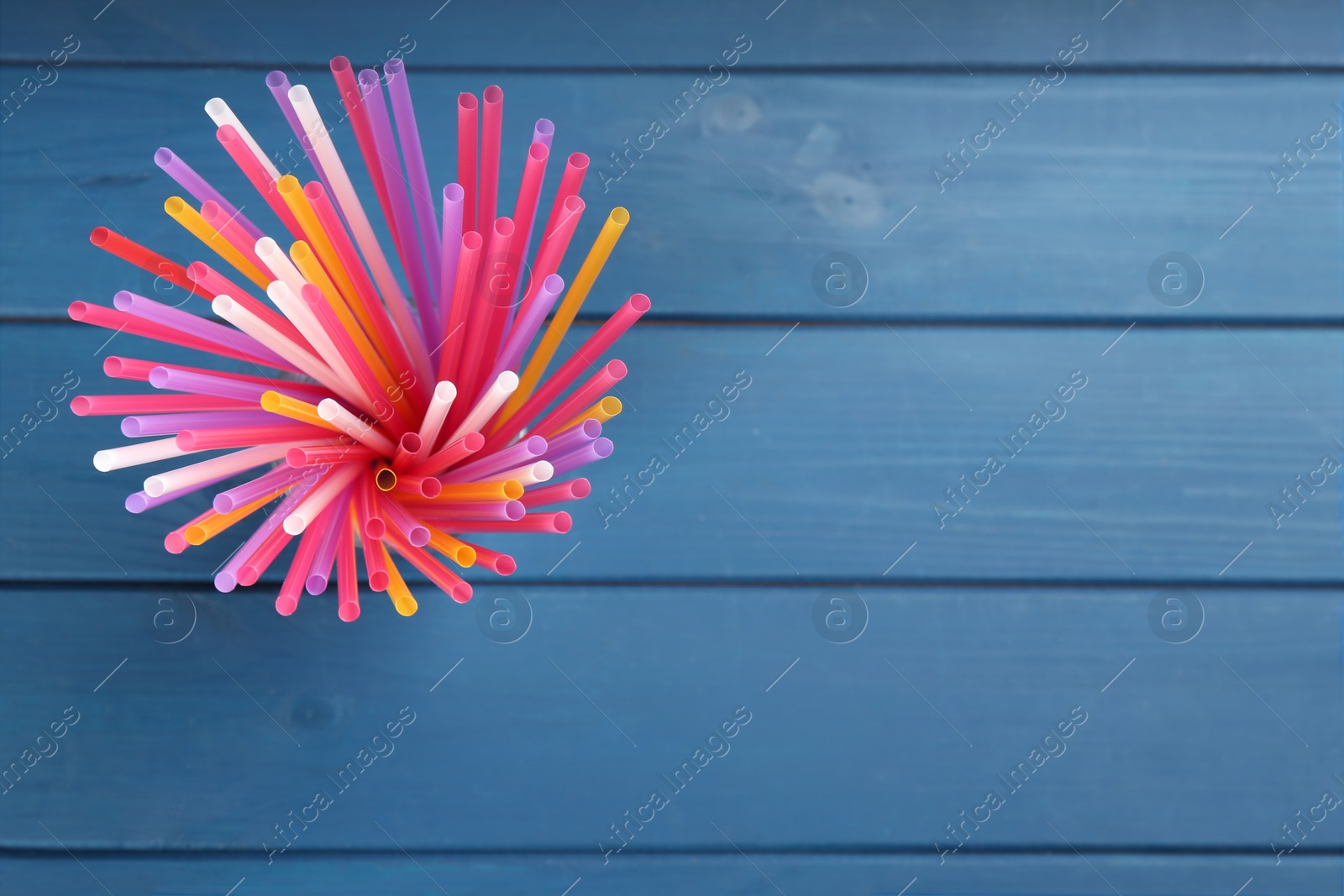 Photo of Colorful plastic drinking straws on blue wooden table, top view. Space for text