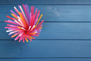 Photo of Colorful plastic drinking straws on blue wooden table, top view. Space for text