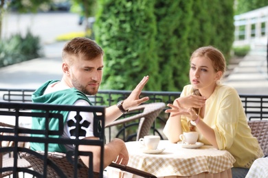 Photo of Young couple arguing while sitting in cafe, outdoors. Problems in relationship