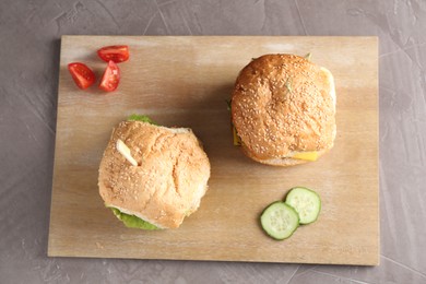 Photo of Board with delicious vegetarian burgers on grey textured table, top view