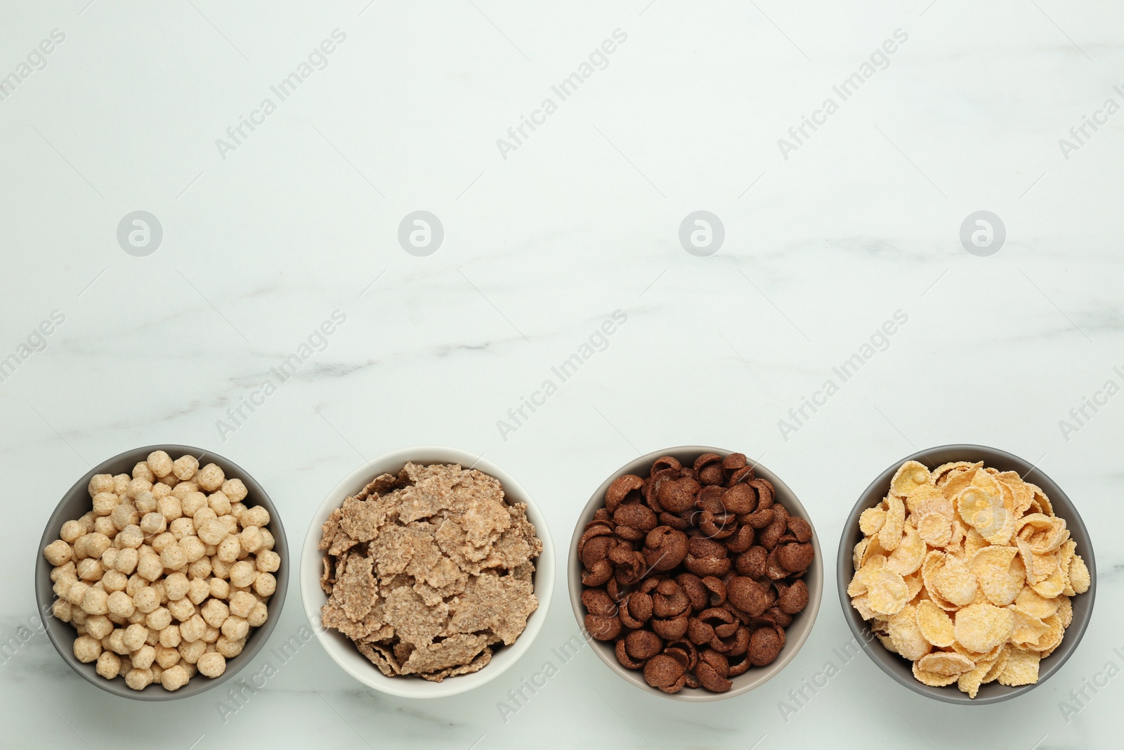 Photo of Different delicious breakfast cereals on white table, flat lay. Space for text