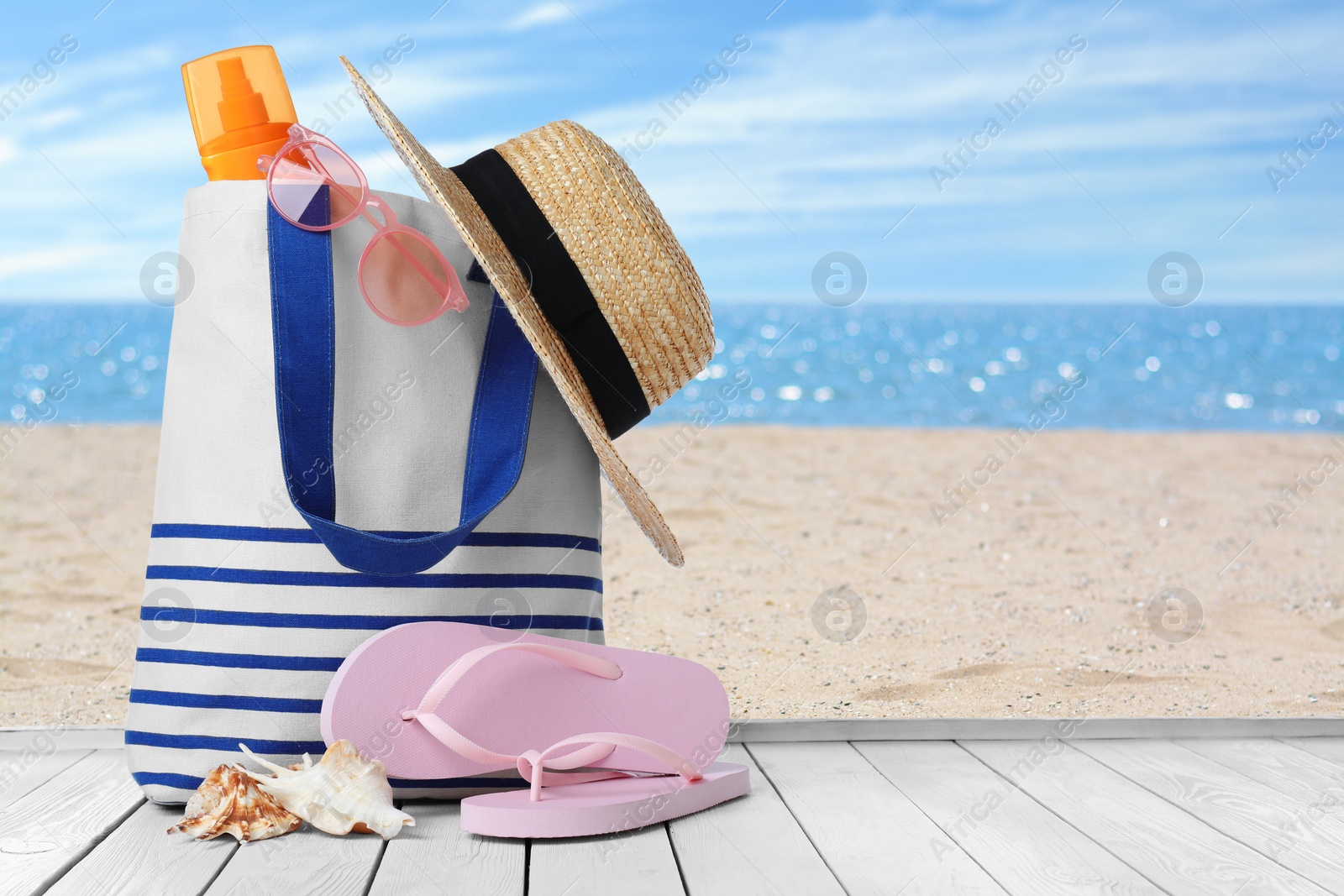 Image of Bag with sunscreen and accessories on sunny ocean beach, space for text. Summer vacation