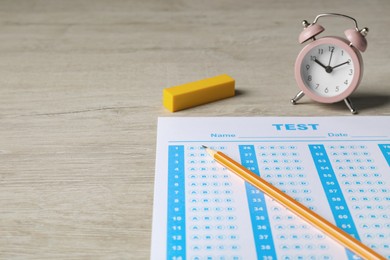 Answer sheet, pencil and alarm clock on wooden table, space for text. Student passing exam