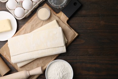 Photo of Raw puff pastry dough and ingredients on wooden table, flat lay. Space for text