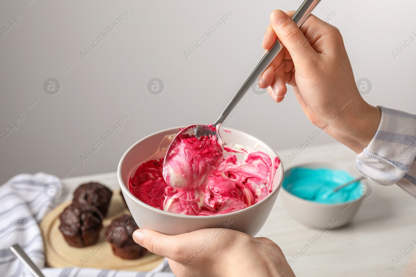 Photo of Woman mixing pink food coloring indoors, closeup. Decorate cupcakes