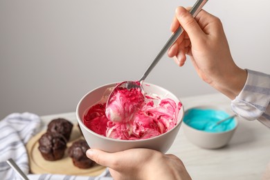 Woman mixing pink food coloring indoors, closeup. Decorate cupcakes