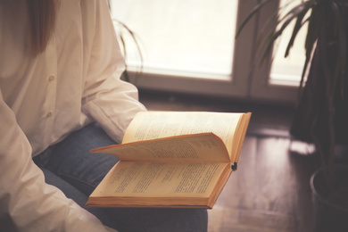 Woman reading book near window indoors, closeup