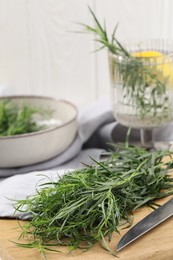 Photo of Fresh tarragon sprigs and knife on wooden board, closeup