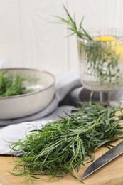 Fresh tarragon sprigs and knife on wooden board, closeup