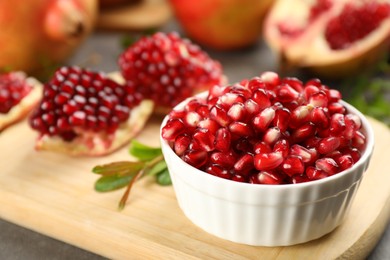 Photo of Delicious ripe pomegranate kernels in bowl on wooden board, closeup. Space for text