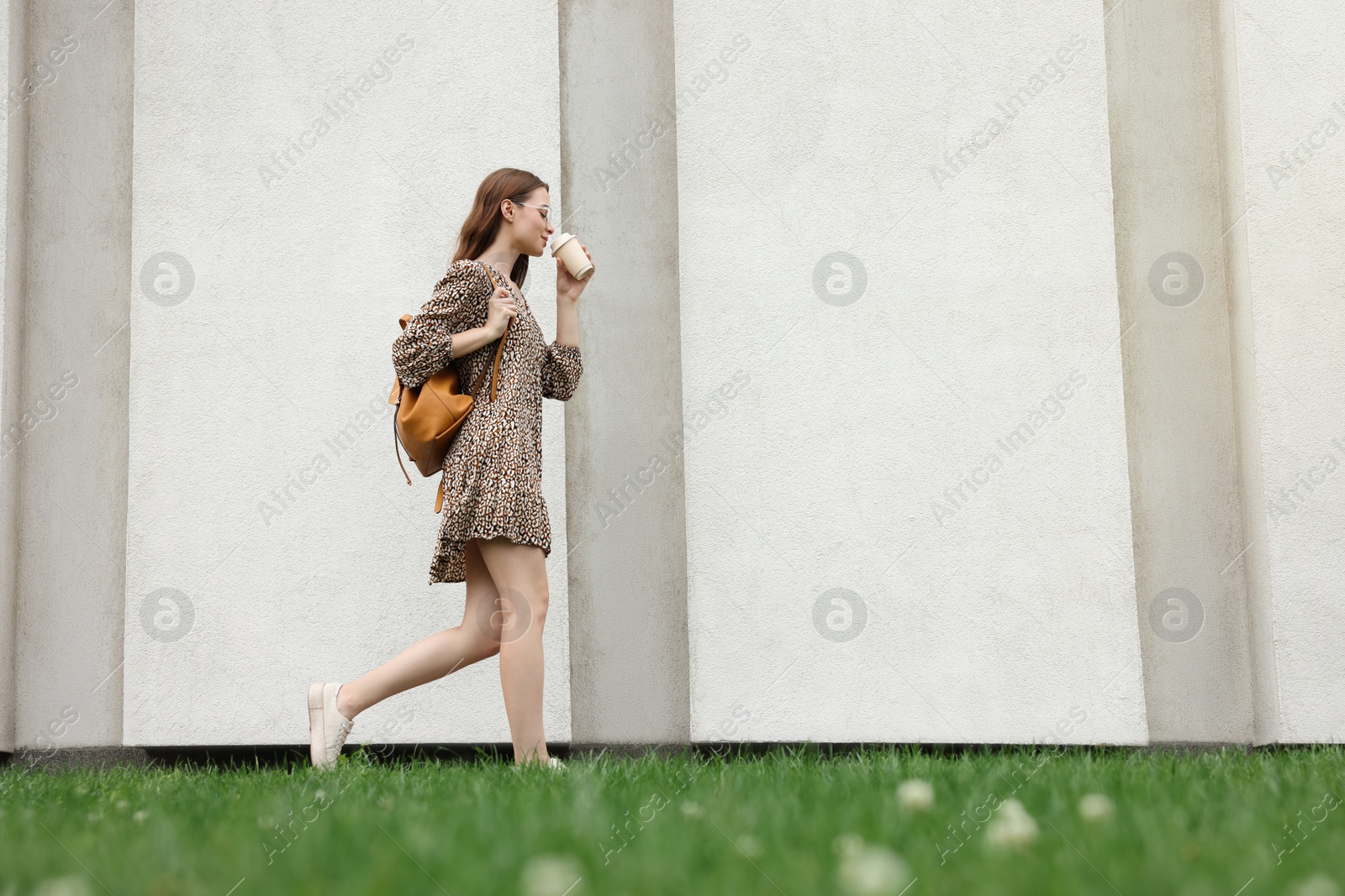 Photo of Young woman with cup of drink walking near stone wall outdoors, space for text